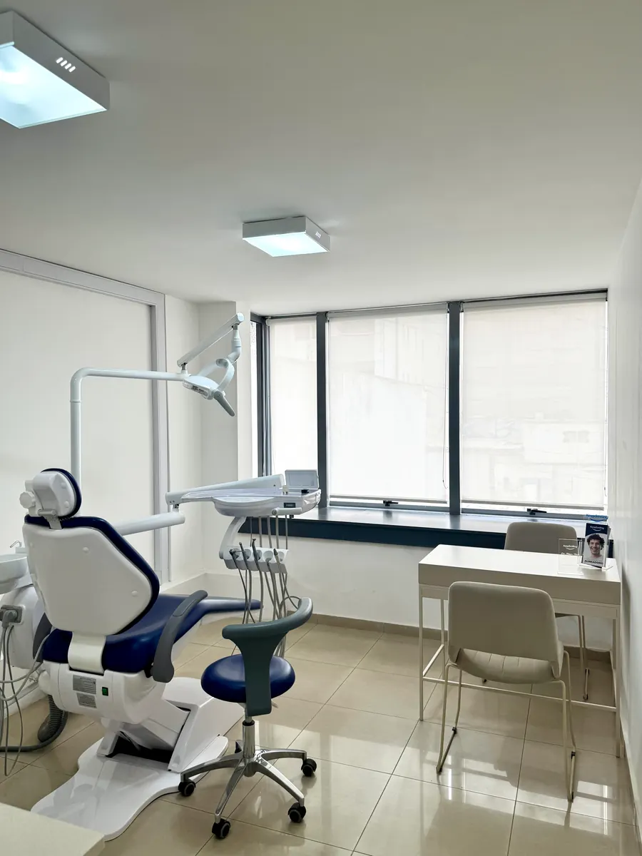 Consultorio de Córdoba: sillón odontológico azul, escritorio y una ventana amplia con cortinas claras.