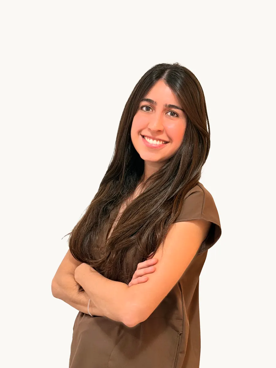 Od. Milagros Olmedo sonriendo, de brazos cruzados, con ambo marrón sobre un fondo claro.